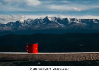 a red mug with tea or coffee stands on a bench against the background of mountains - Powered by Shutterstock