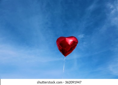 Red Mylar Heart Shaped Valentines Day Helium Filled Balloon Floats Freely Into The Blue Sky With White Clouds. Valentines Day Is Celebrated On February 14 Of Each Year.