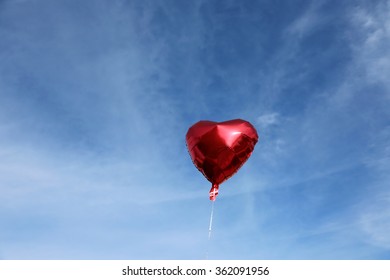 Red Mylar Heart Shaped Valentines Day Helium Filled Balloon Floats Freely Into The Blue Sky With White Clouds. 