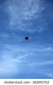 Red Mylar Heart Shaped Valentines Day Helium Filled Balloon Floats Freely Into The Blue Sky With White Clouds. Valentines Day Is Celebrated On February 14 Of Each Year.