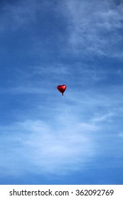 Red Mylar Heart Shaped Valentines Day Helium Filled Balloon Floats Freely Into The Blue Sky With White Clouds. Valentines Day Is Celebrated On February 14 Of Each Year.