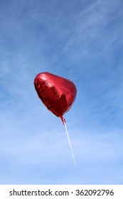 Red Mylar Heart Shaped Valentines Day Helium Filled Balloon Floats Freely Into The Blue Sky With White Clouds. Valentines Day Is Celebrated On February 14 Of Each Year.