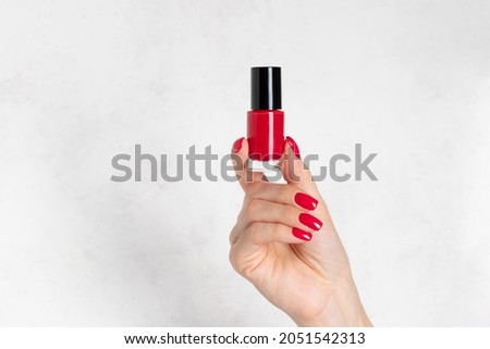 red nail polish bottle in a female hand with red manicure. hand skin care concept. Template for advertising. white background with copy space.