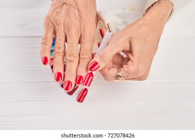 Red Nail Sample In Female Hand. Old Woman Hand With Red Manicure Holding Red Nail Sample. Well-groomed Femal Hands In Beauty Salon.