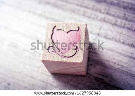 Red Naugthy Heart With Devil Horns And Tail Engraved On A Wooden Block On A Table
