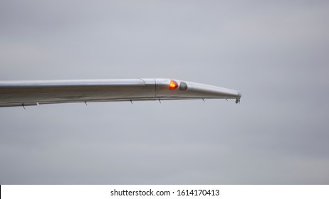 Red Navigation Light On Left Wing Of Jet Airplane, Cloudy Sky.