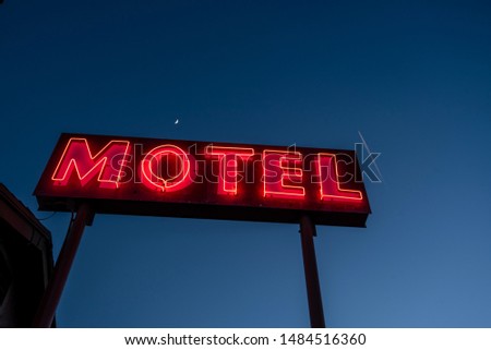 red neon letters of mid-century modern MOTEL sign against deep blue sky