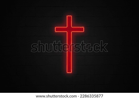 Red neon light shaped into a Christian cross attached on a black brick wall.