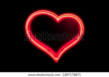 Red neon light shaped into a heart isolated on black background.