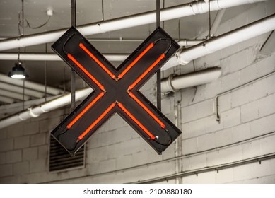A red neon sign in the shape of an X to indicate the wrong way to enter a downtown parking lot.