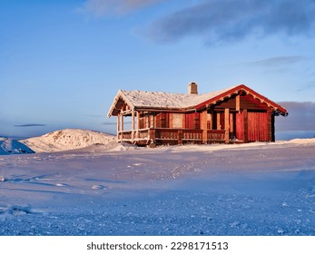 A red Norwegen timber house in a frozen landscape during a winter sunrise in Eidfjord, Norway