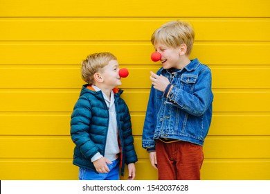 Red Nose Day Concept. Happy Little Brothers Looks At Each Other Wearing Red Clown Noses Having Fun Together On Sunny Autmn Day Outdoor, Yellow Background. Two Kid Playing Together. Red Nose Day