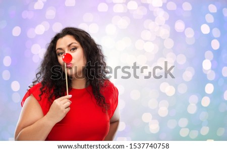 red nose day, party props and photo booth concept - happy woman with clown nose posing over festive lights background