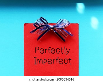 Red note with blue ribbon on blue background with handwritten text PERFECTLY  IMPERFECT, concept of accept yourself no matter what, with all flaws, imperfections make life interesting and help us grow