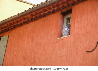 Red Ocher Wall Of An Old House. The Window Is Decorated With A Large White Vase With Blue Ornaments. Mass Production Vase. Copy Space.