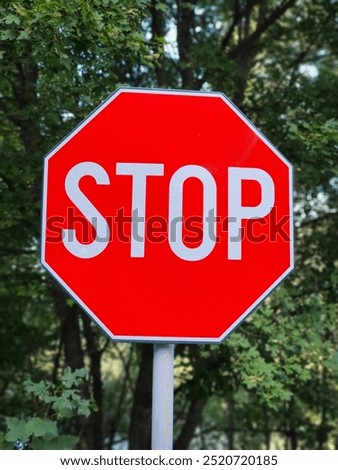 Red octagonal stop sign with white lettering against a lush green forest backdrop.