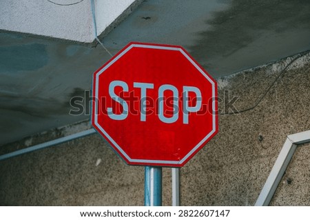 Red octagonal STOP traffic sign with white letters on metal pole against textured concrete wall under overhang