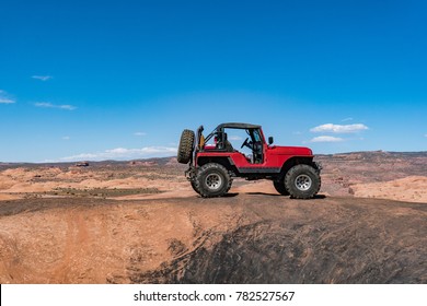 Red off road vehicle sits on top of slick rock in Moab Utah with blue sky in the background - Powered by Shutterstock