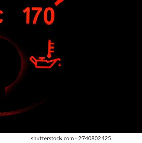 Red oil pressure warning light icon on a car dashboard. Engine oil temperature symbol illuminated in dark background.