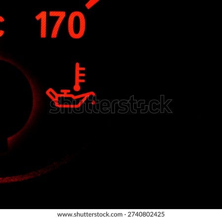 Red oil pressure warning light icon on a car dashboard. Engine oil temperature symbol illuminated in dark background.