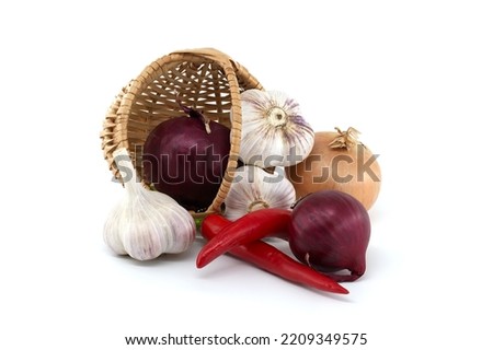 Red onions, red chili pepper and garlic bulbs falls out from wicker basket. Spices and flavoring theme still life isolated on white background