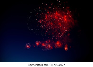 Red and orange fireworks with green sparks inside and smoke, below you can see small fireworks against the night sky. High quality photo