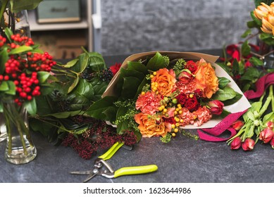 Red and orange flower bouquet on stone surface. An assembled bouquet of flowers in paper packaging next to scissors or a florist pruner.