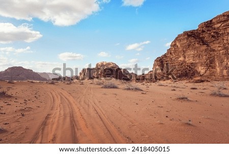 Red orange sandstone rocks formations in Wadi Rum desert, vehicle tire prints in sand road near