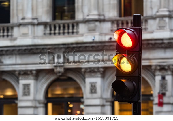 Red and orange traffic lights for cars on a\
blurred buildings background \
