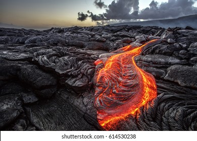 Red Orange vibrant Molten Lava flowing onto grey lavafield and glossy rocky land near hawaiian volcano with vog on background - Shutterstock ID 614530238