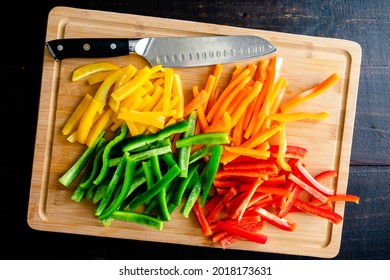 Red, Orange, Yellow, and Green Bell Peppers Cut into Thin Strips: Bell peppers cut in batonnets on a bamboo cutting board with a chef's knife - Shutterstock ID 2018173631