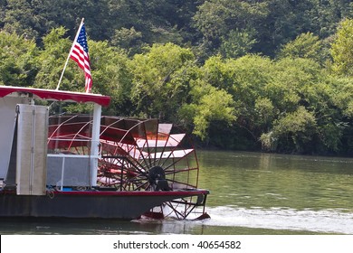 A red paddle wheel on a river boat cruising down a river with an American flag - Powered by Shutterstock