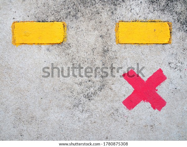 red paint cross marks on cement floor of train\
station platform with yellow dividing line, symbol for passengers\
stand to wait for train and keep distance, social distancing\
concept, close up top view