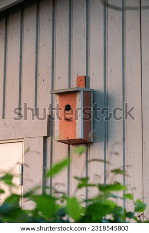 Red painted bird house on the side of a garage.