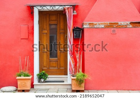 Red painted facade of the house and wooden door with flowers. Colorful architecture in Burano island, Venice, Italy.