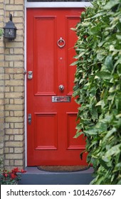 A Red Painted Front Entrance Door Behind A Hedge To An Old House In West London, UK.