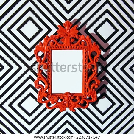 Red painted ornate frame against retro style wallpaper. Creative copy space. Eclectic style idea.