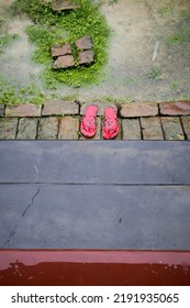 A Red Pair Of Slippers In Front Of A House In The Rain. Bricks Made Stairs And Pathways Can Be Seen In The Picture.