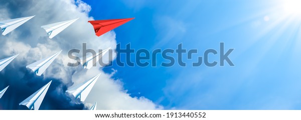 Red Paper Airplane Leading Fleet Of Small White\
Planes Away From Approaching Storm Toward Blue Sky And Sun -\
Leadership Concept