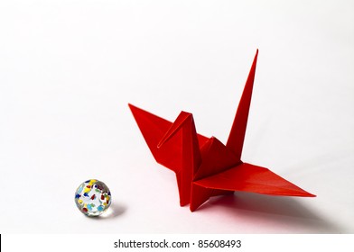 A Red Paper Crane And A Marble With White Background