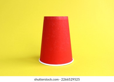 A red paper glass stands upside down on a yellow background.