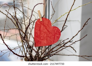 Red Paper Heart Or Crumpled Heart Attached By Tree Branches From A Vase, In The House. Heart Attached With Wooden Clothes Pin. Home Decoration. Dry Branches. Blue Background Or Near The Window. Love, 