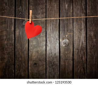 Red paper heart hanging on the clothesline. On old wood background.
