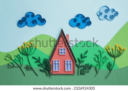 Red paper house with blue windows and garden isolated on a green and blue paper background. Small house made in quilling technique. Hand made of paper. Home sweet home in a summer happy day.