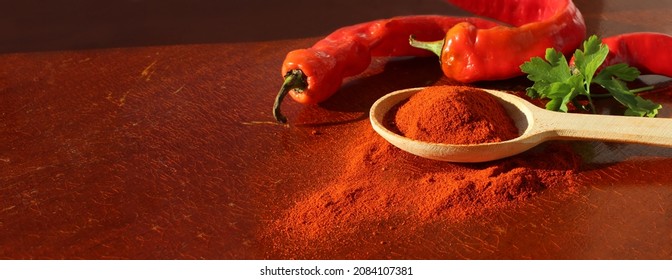 Red paprika seasoning in wooden spoon side view next to peppercorns on wooden red cracked background