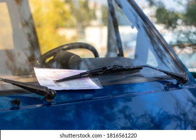 Red parking ticket stuck under the windshielf wiper of a blue car, person fined for illegal parking in public. Contents of the ticket blurred for privacy - Shutterstock ID 1816561220