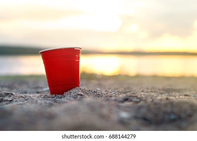 Red Party Cup In Sand At Sunset. Summer Beach Party Concept With Copy Space.