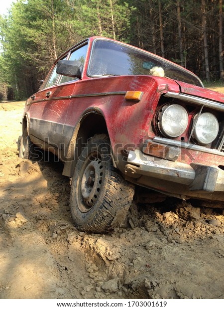 A red passenger car stuck deep in the mud on a\
forest road.