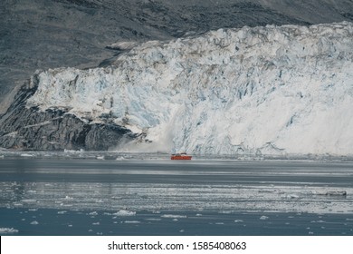 Red Passenger Cruise Ship Sailing Through The Icy Waters Of Qasigiannguit, Greenland With Eqip Sermia Eqi Glacier In Background. Ice Breaking Off From Calving Glacier. A Small Boat Among Icebergs