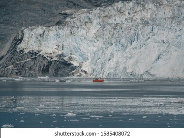 Red Passenger Cruise Ship Sailing Through The Icy Waters Of Qasigiannguit, Greenland With Eqip Sermia Eqi Glacier In Background. Ice Breaking Off From Calving Glacier. A Small Boat Among Icebergs